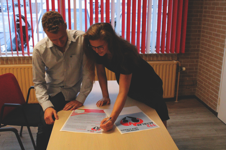 Twee personen bekijken en bespreken posters aan een tafel in een zakelijke omgeving.