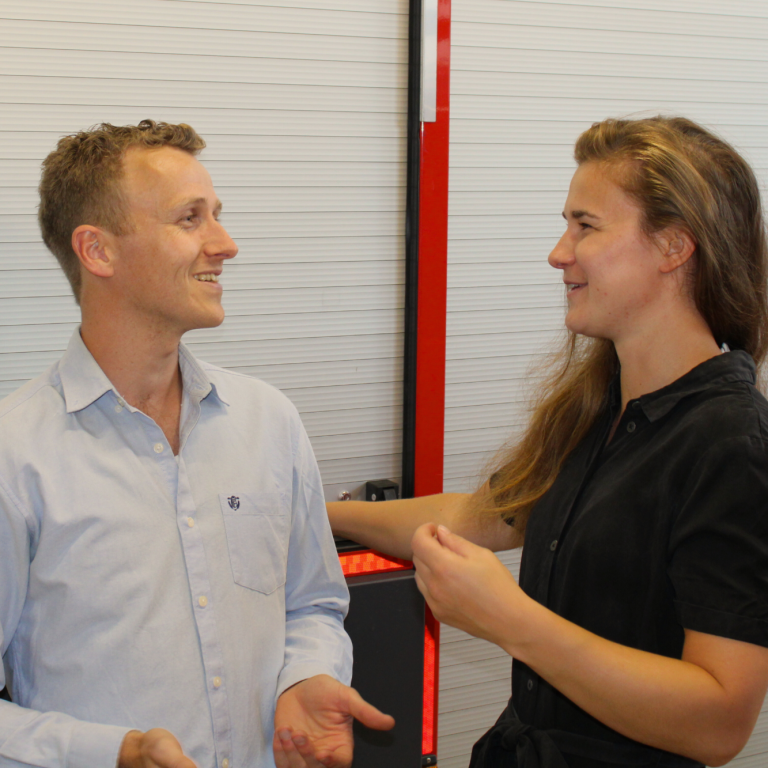 Twee mensen in gesprek, een man in een lichtblauw shirt en een vrouw in een zwarte jurk. Ze discussiëren.