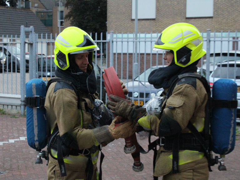 Twee brandweermannen in beschermende uitrusting wisselen slang uit.